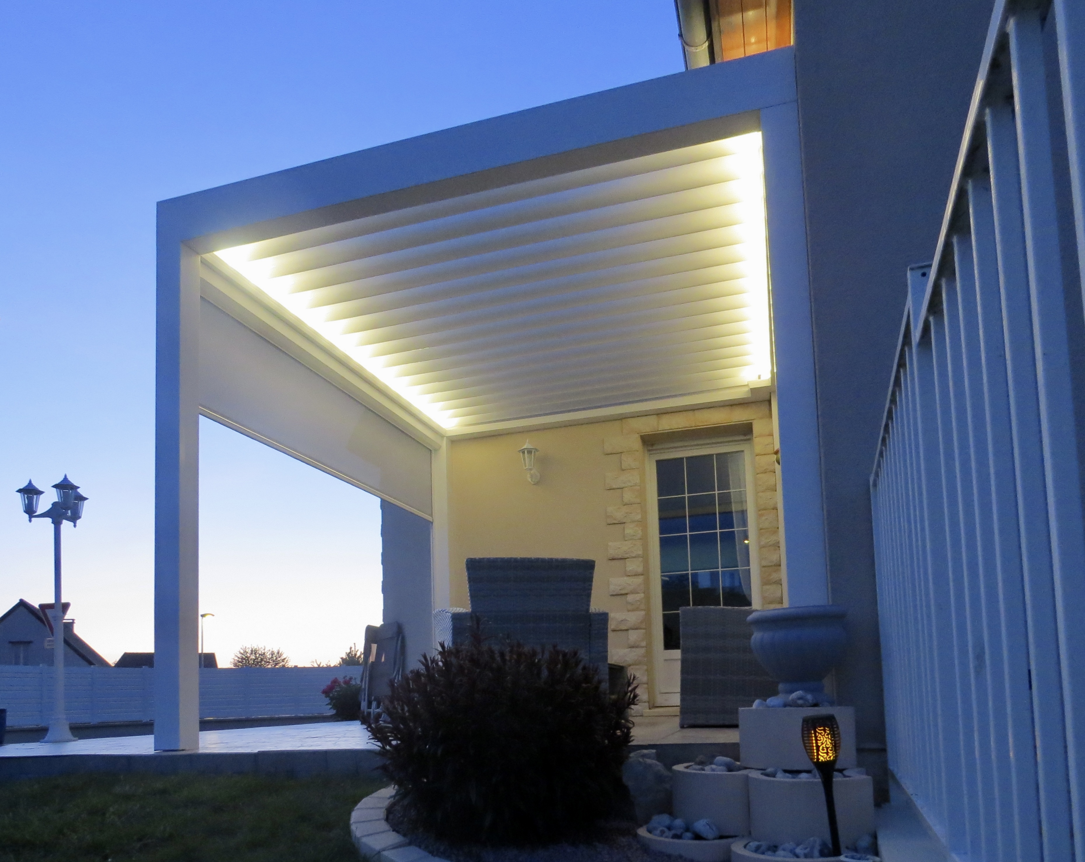 Pergola éclairée devant maison au crépuscule.