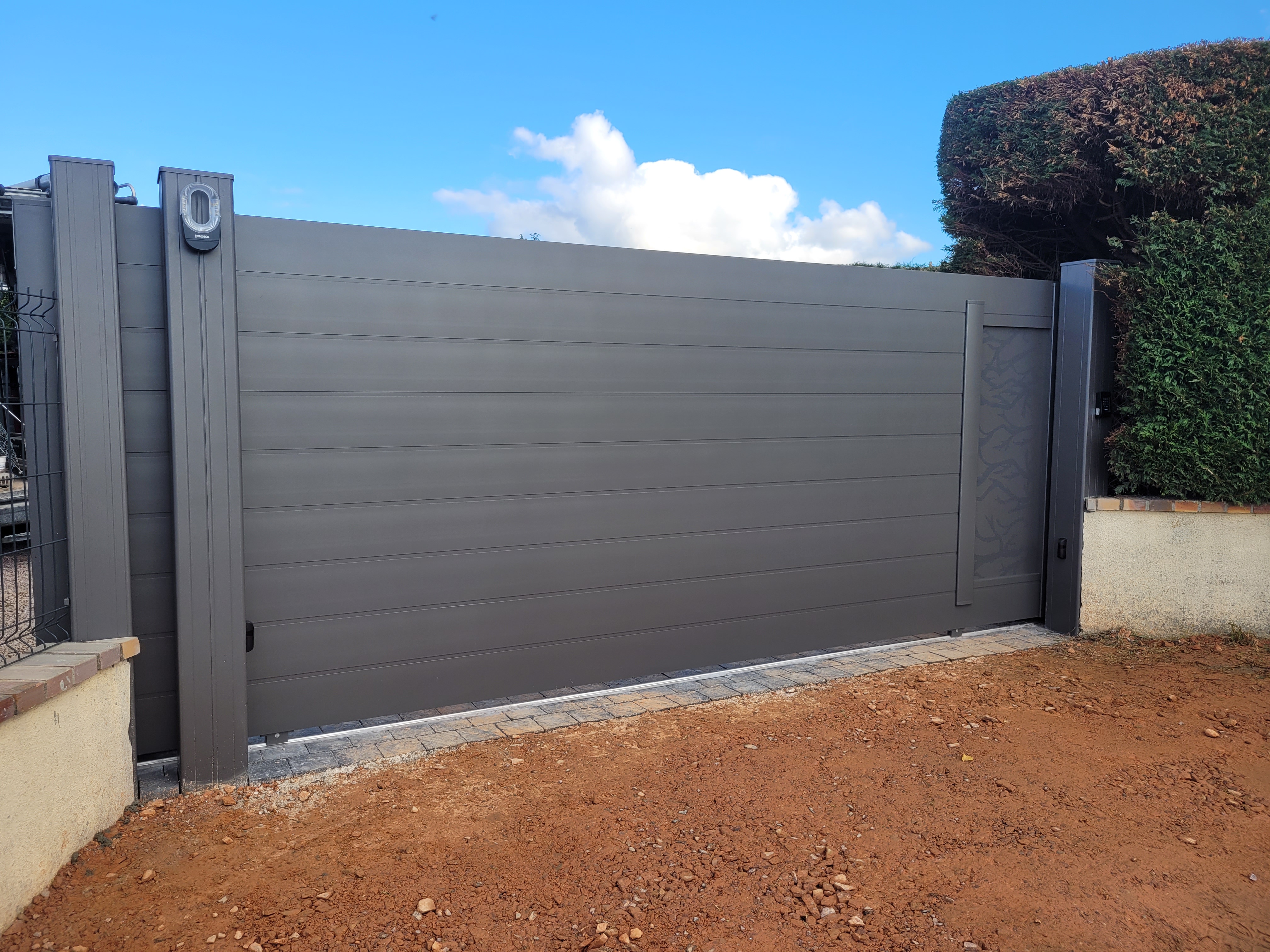 Portail moderne gris devant haie taillée.