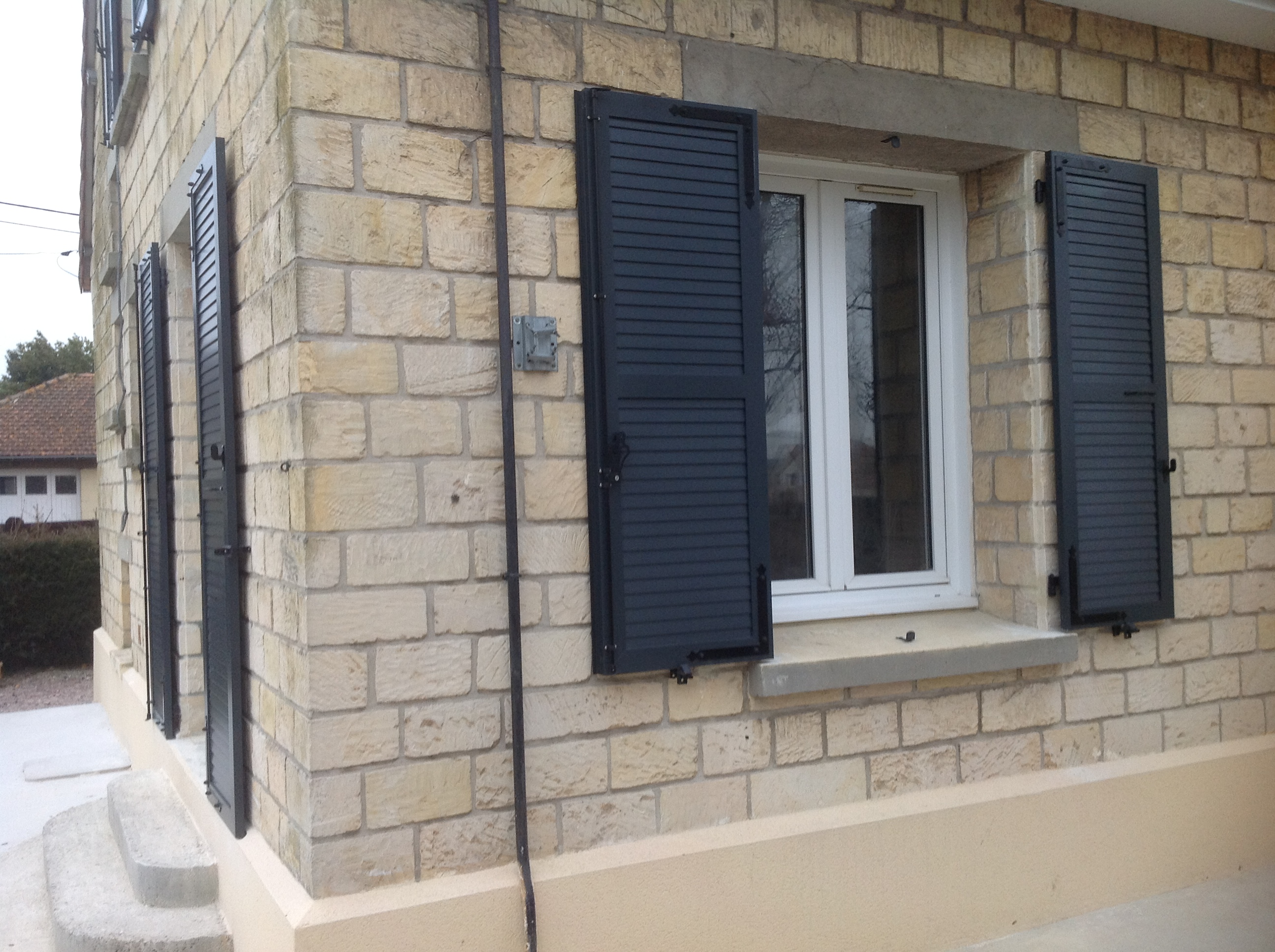 Maison en pierre avec volets noirs ouverts.