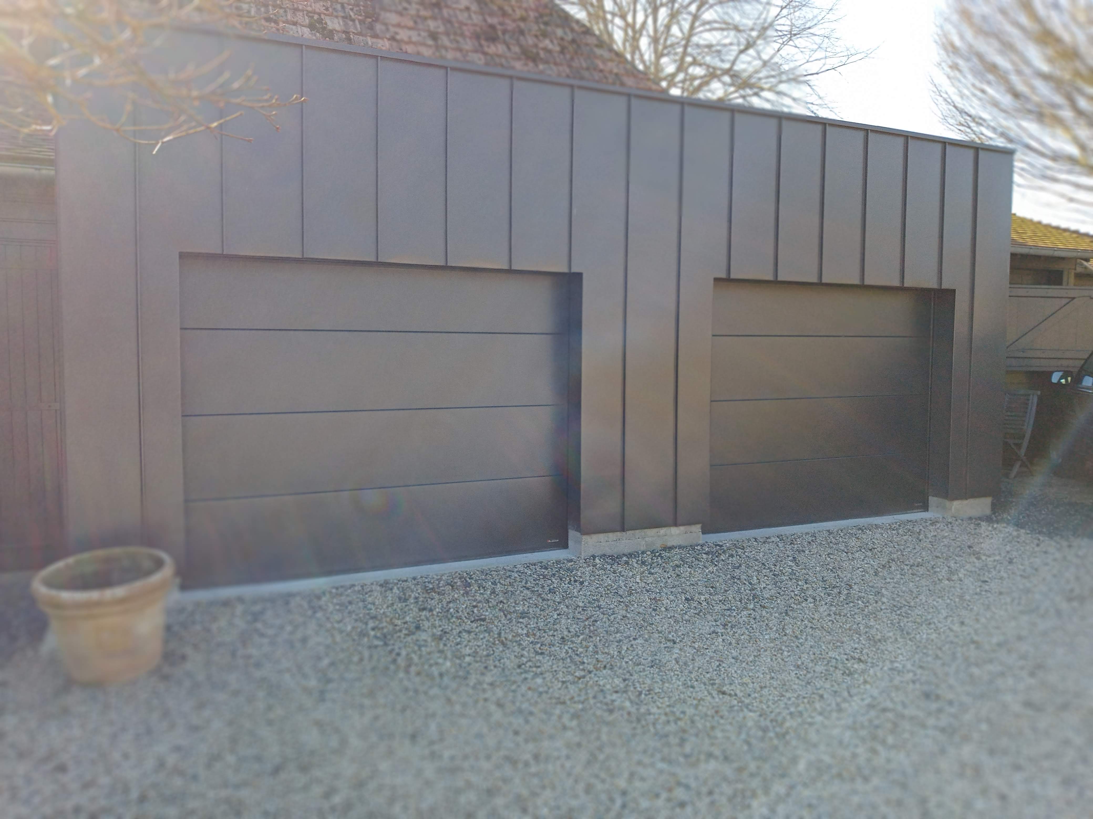 Porte de garage moderne en acier gris, allée gravillonnée.