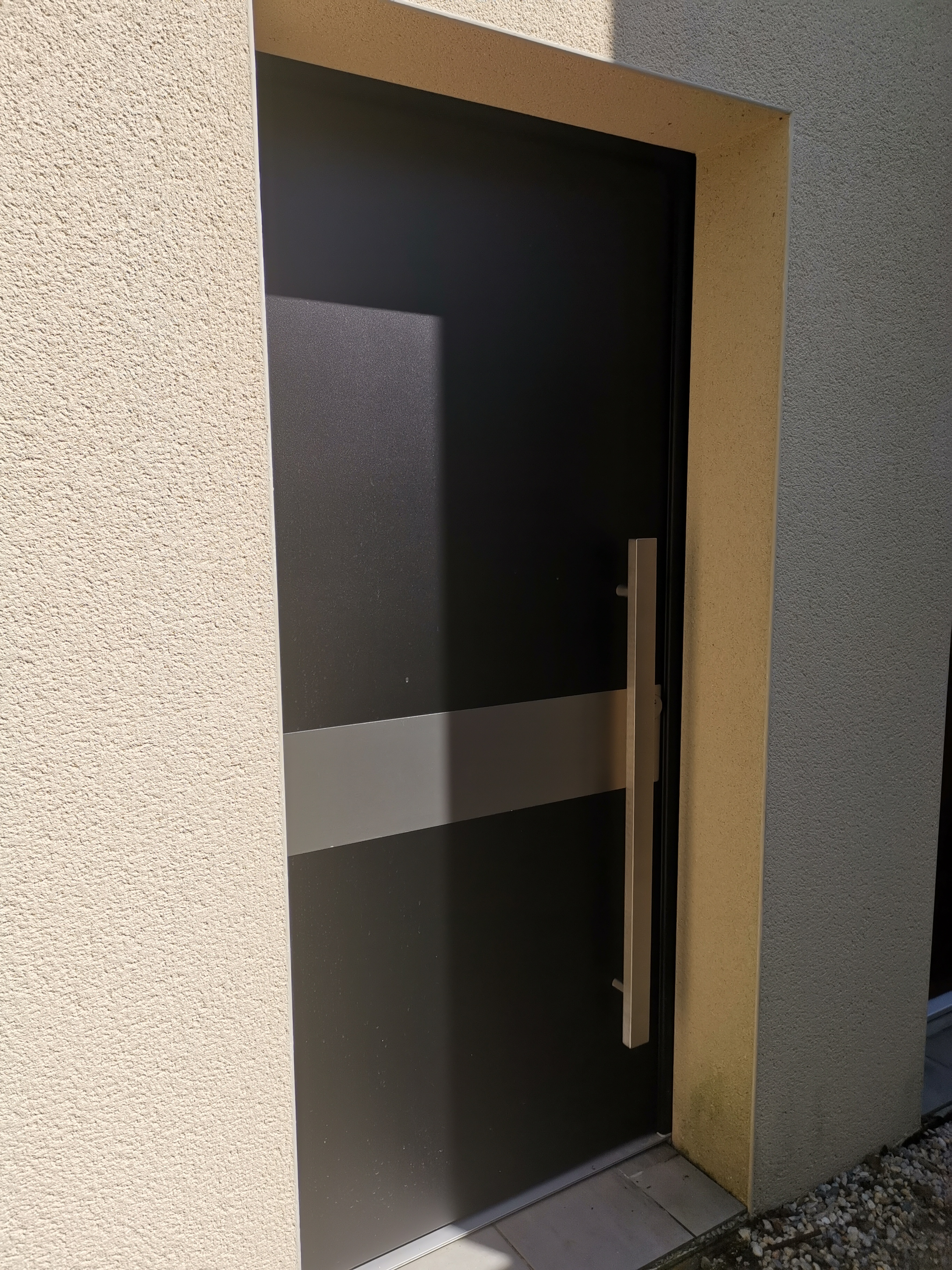 Porte d'entrée grise, ombragée, mur beige