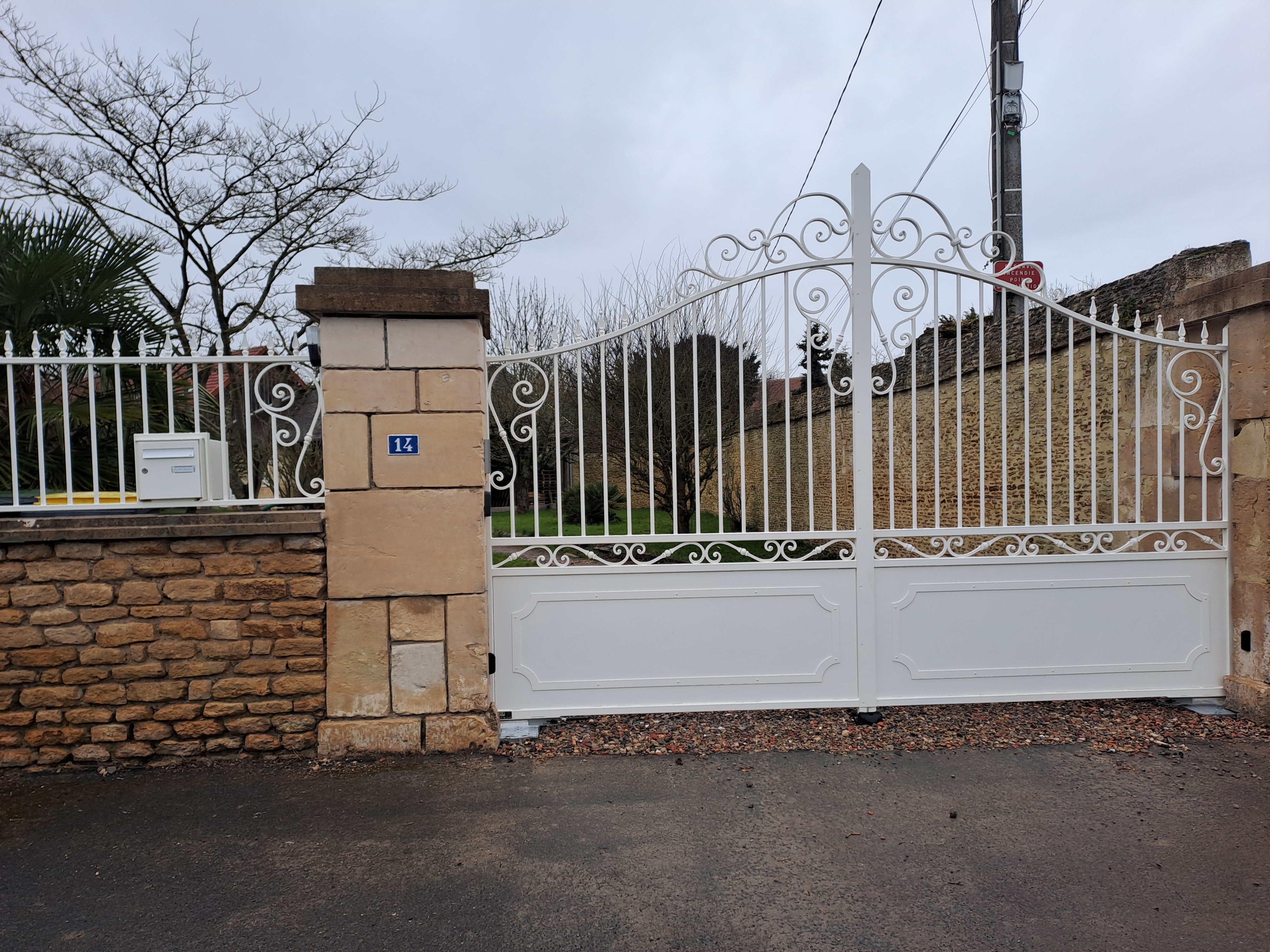 Portail blanc devant une maison en pierre.