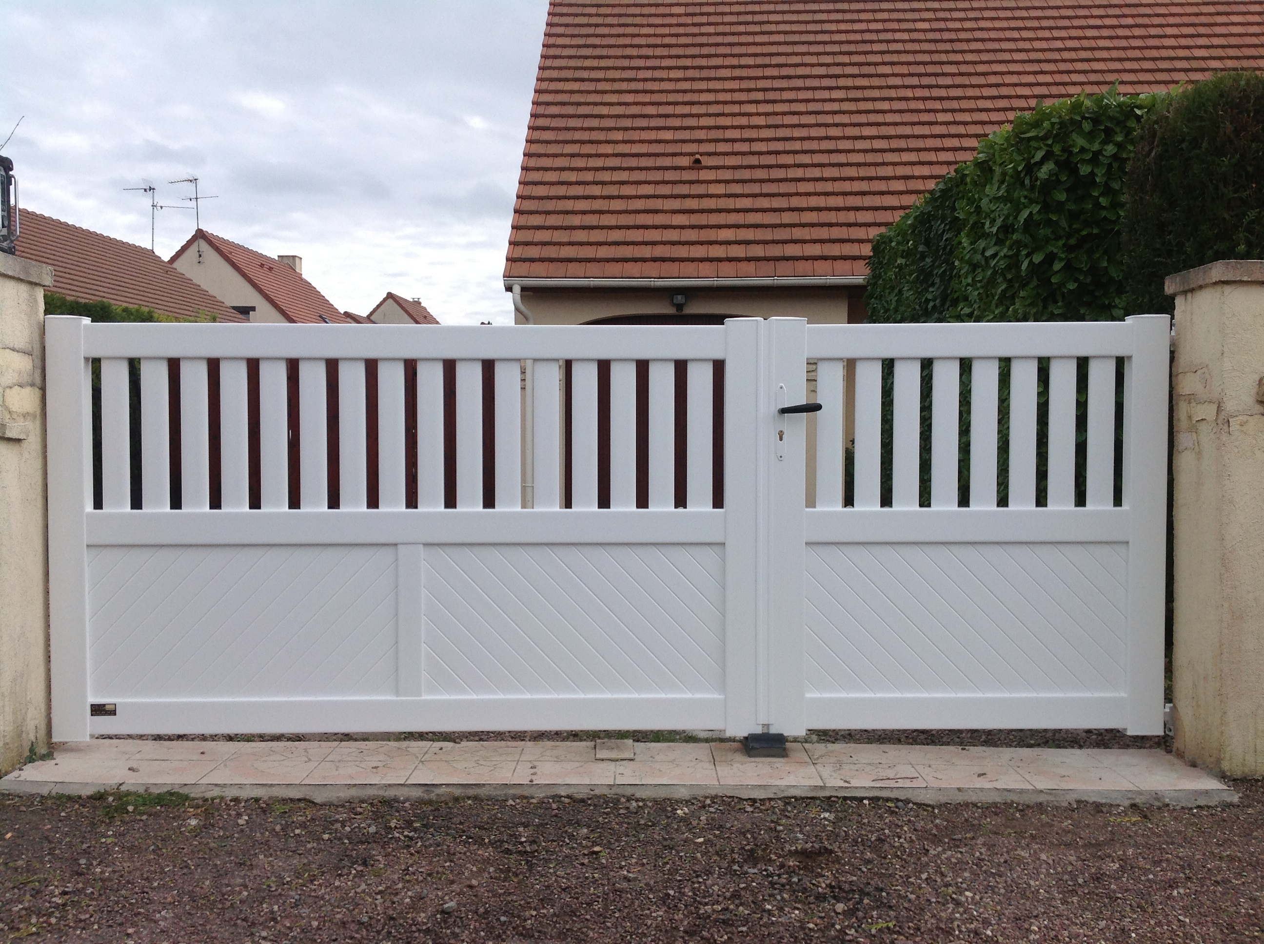 Portail blanc devant maison en briques rouges.