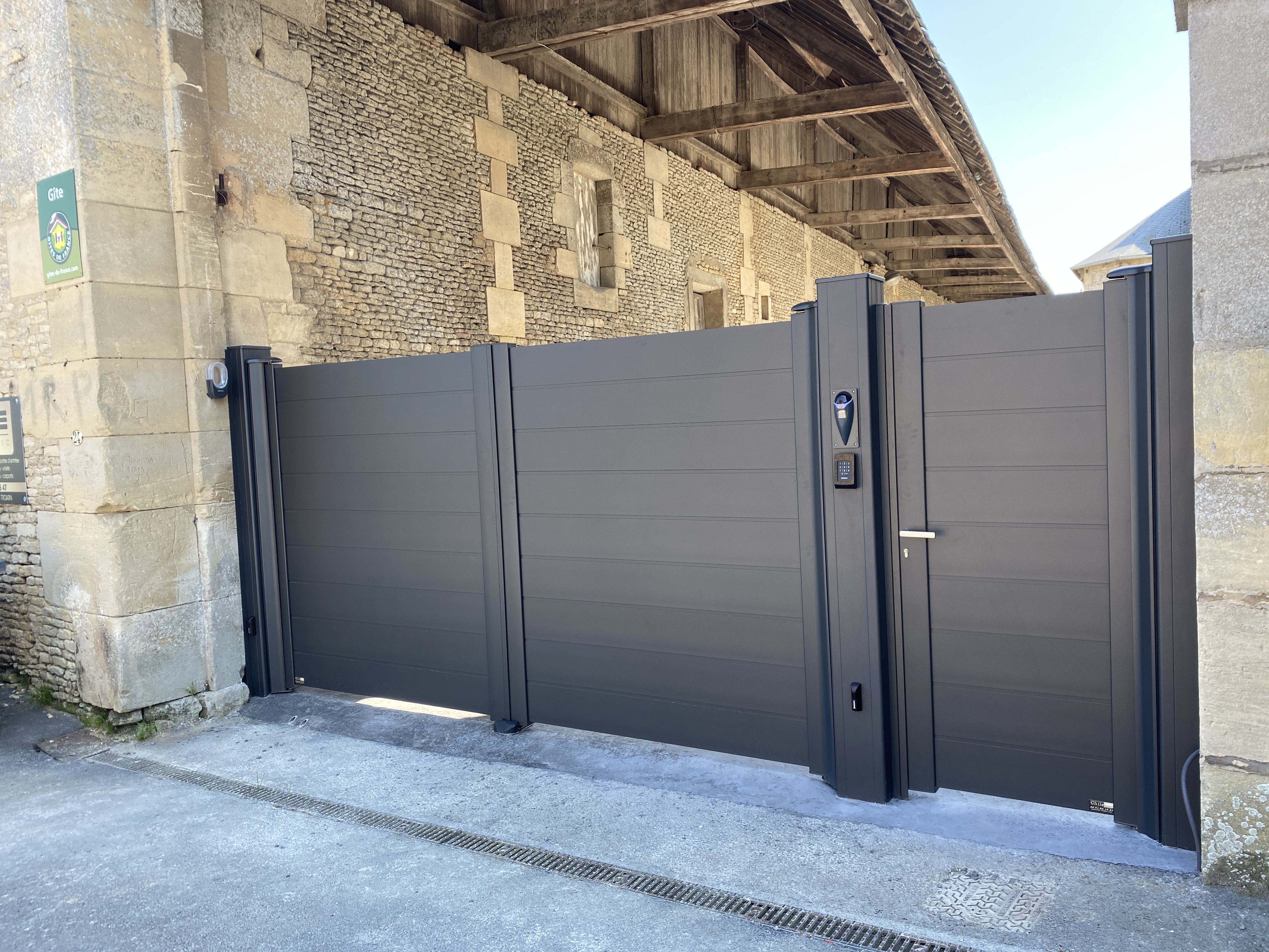 Clôture moderne gris foncé devant bâtiment en pierre.